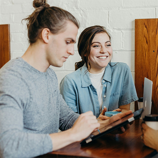 Three coworkers are gathered at a table, working with a laptop.