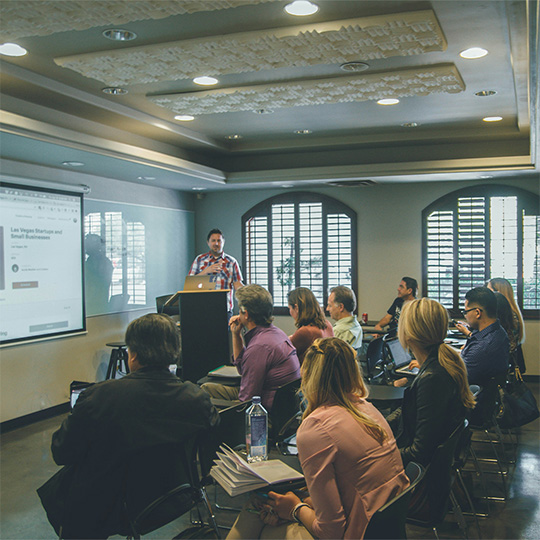 A speaker delivers a presentation to an attentive group, highlighting key points with visual aids in a professional setting.