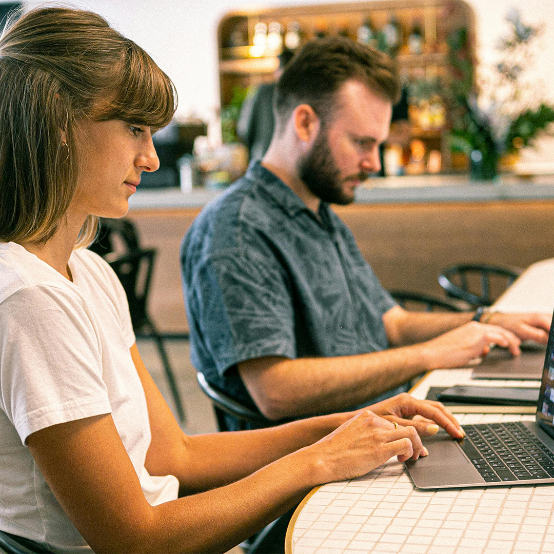 A man and a woman are at a table, both using laptops, illustrating teamwork and collaboration in a modern workspace.