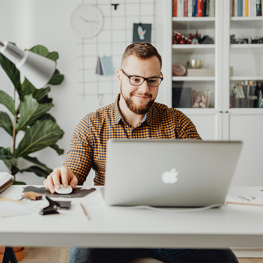 A man wearing glasses is seated at a desk, focused on his laptop while working.