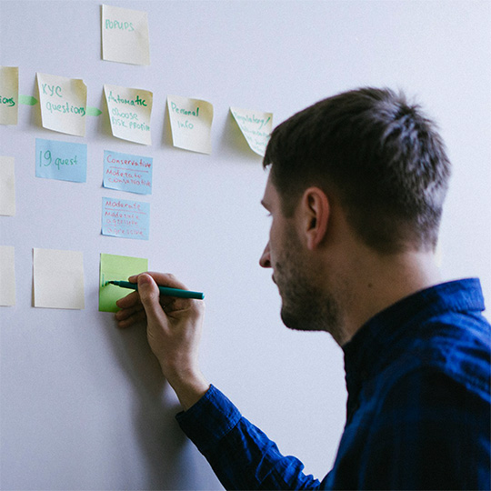 A man creatively arranges colorful sticky notes on a wall, engaged in a writing project.