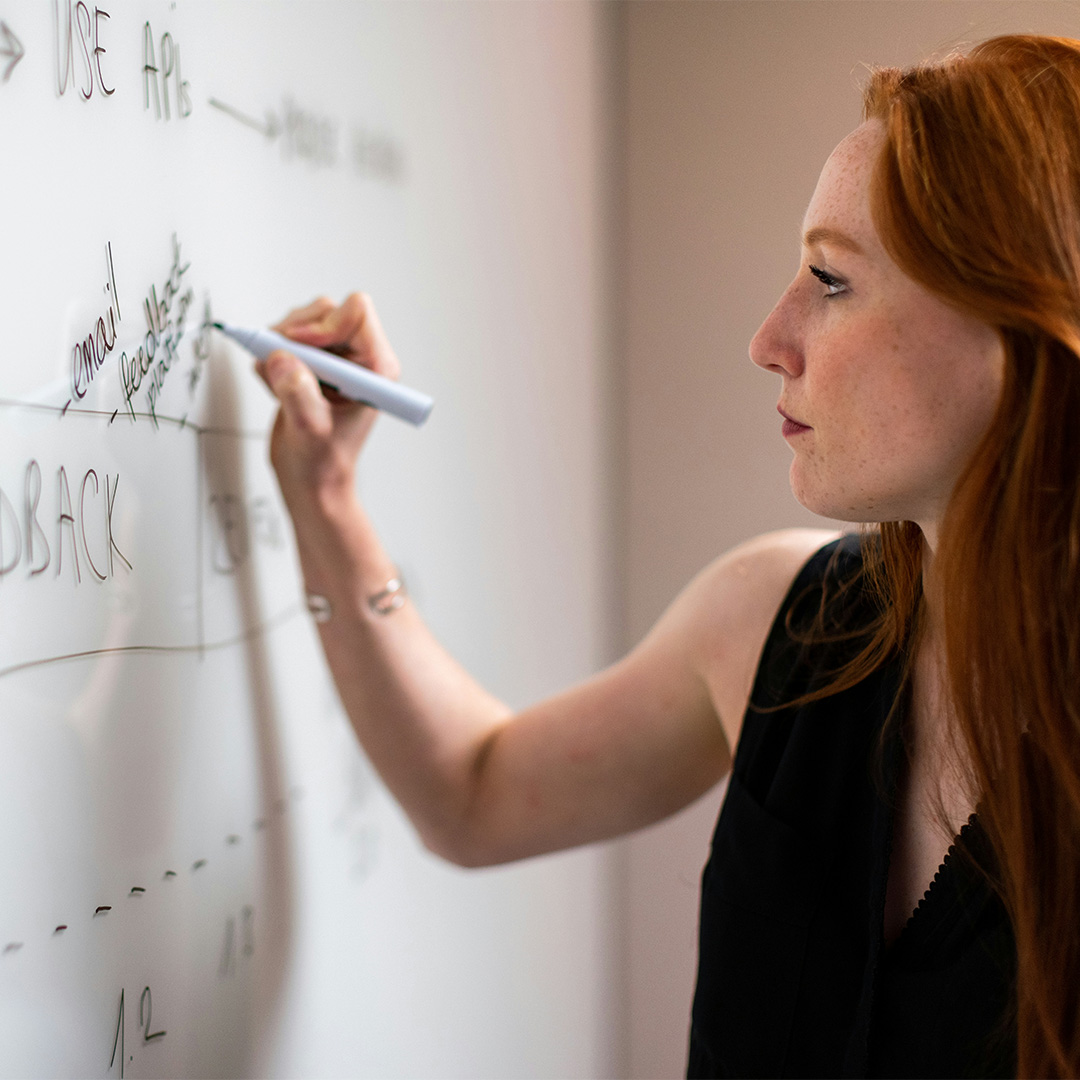 A woman actively writing on a whiteboard, engaged in a brainstorming session or presentation.