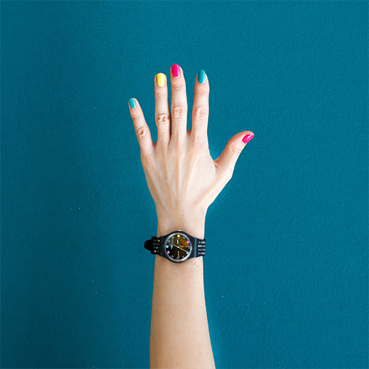 A close-up of a person's hand showcasing vibrant, colorful nails against a neutral background.