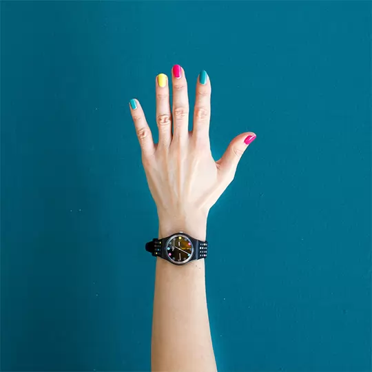 A close-up of a person's hand showcasing vibrant, colorful nails against a neutral background.